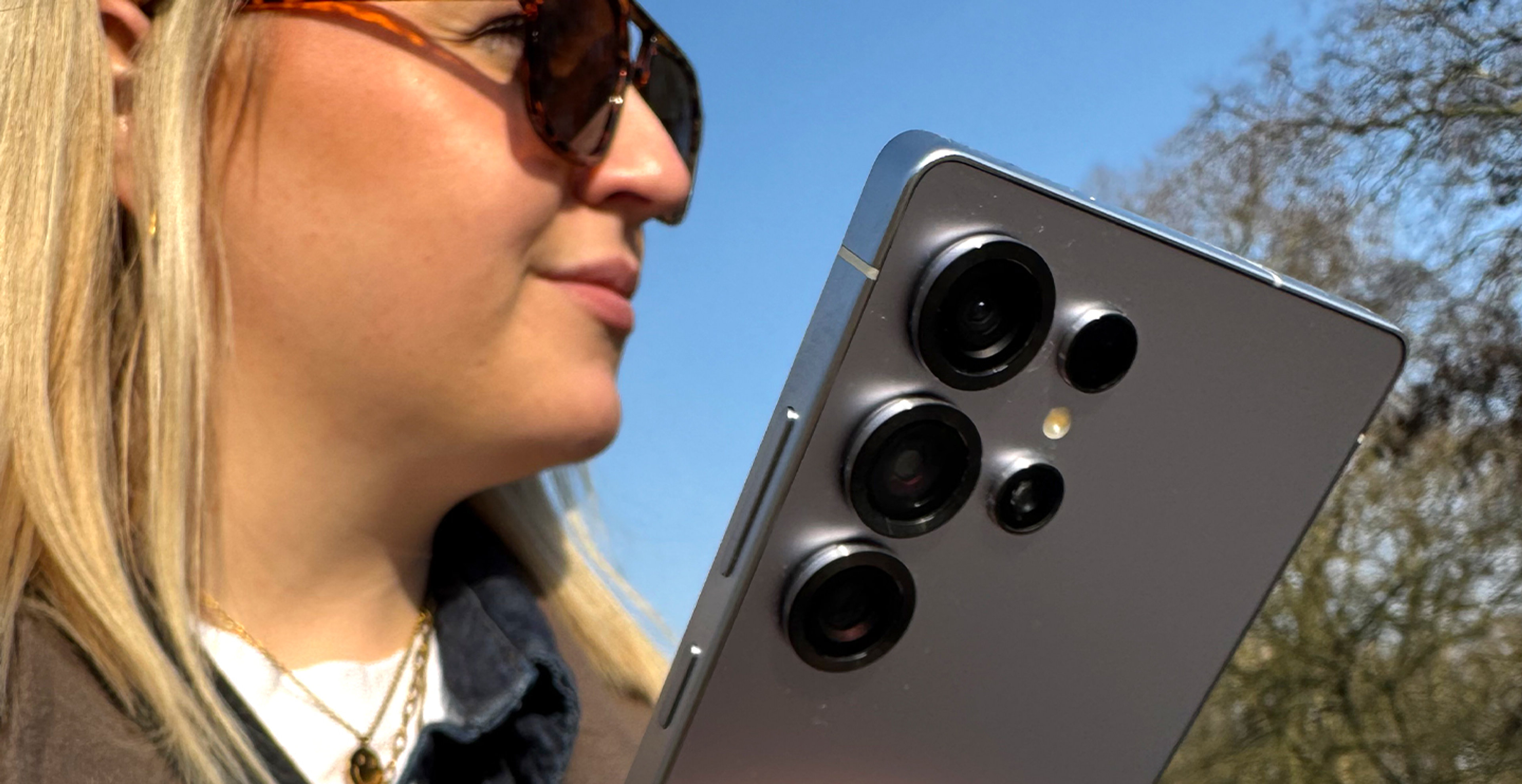 Eine blonde Frau hält lächelnd das Samsung Galaxy S25 Ultra in der Hand. Die Rückseite des Smartphones steht im Fokus.